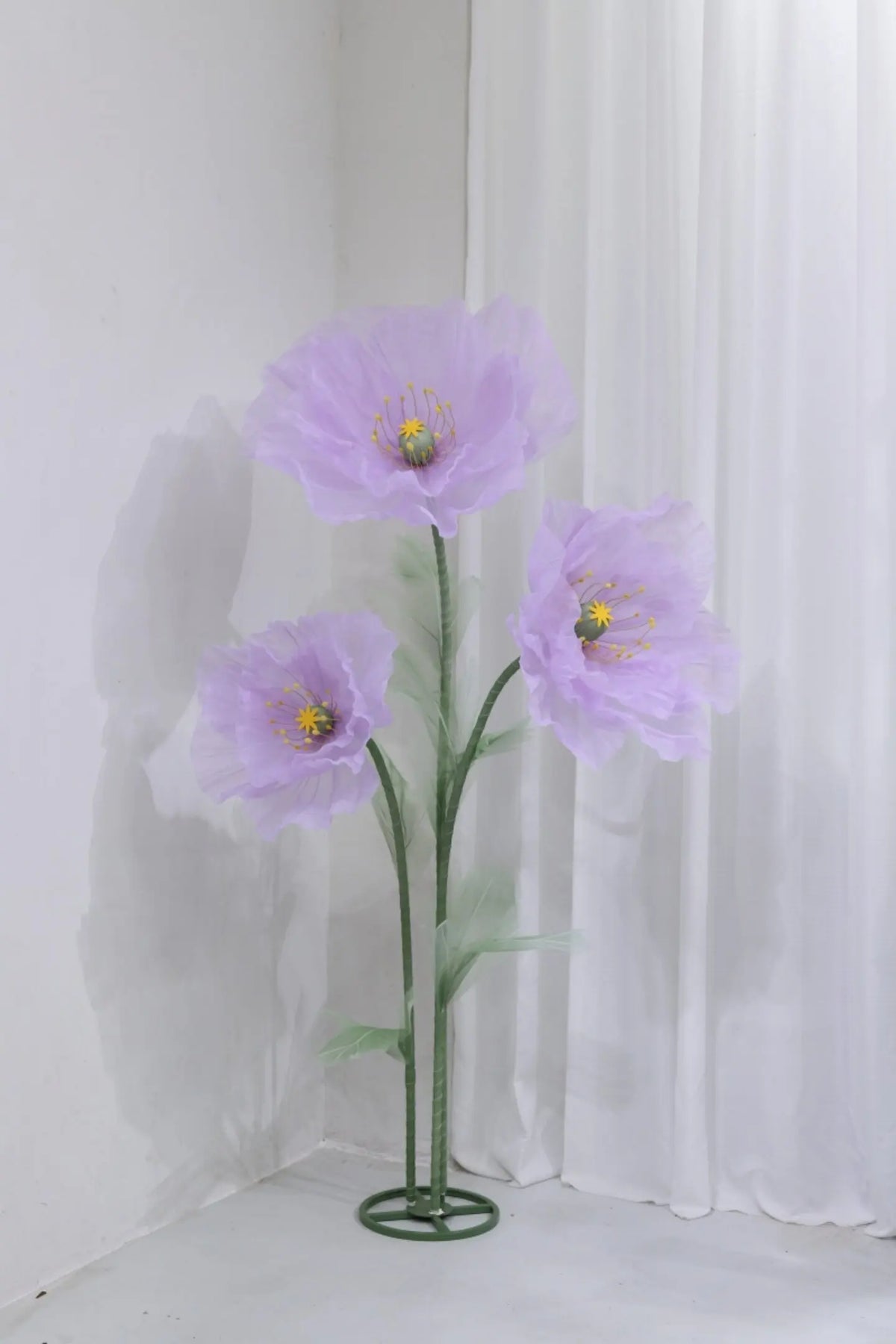 A large artificial silk purple poppy flower with a green stand against a white background.