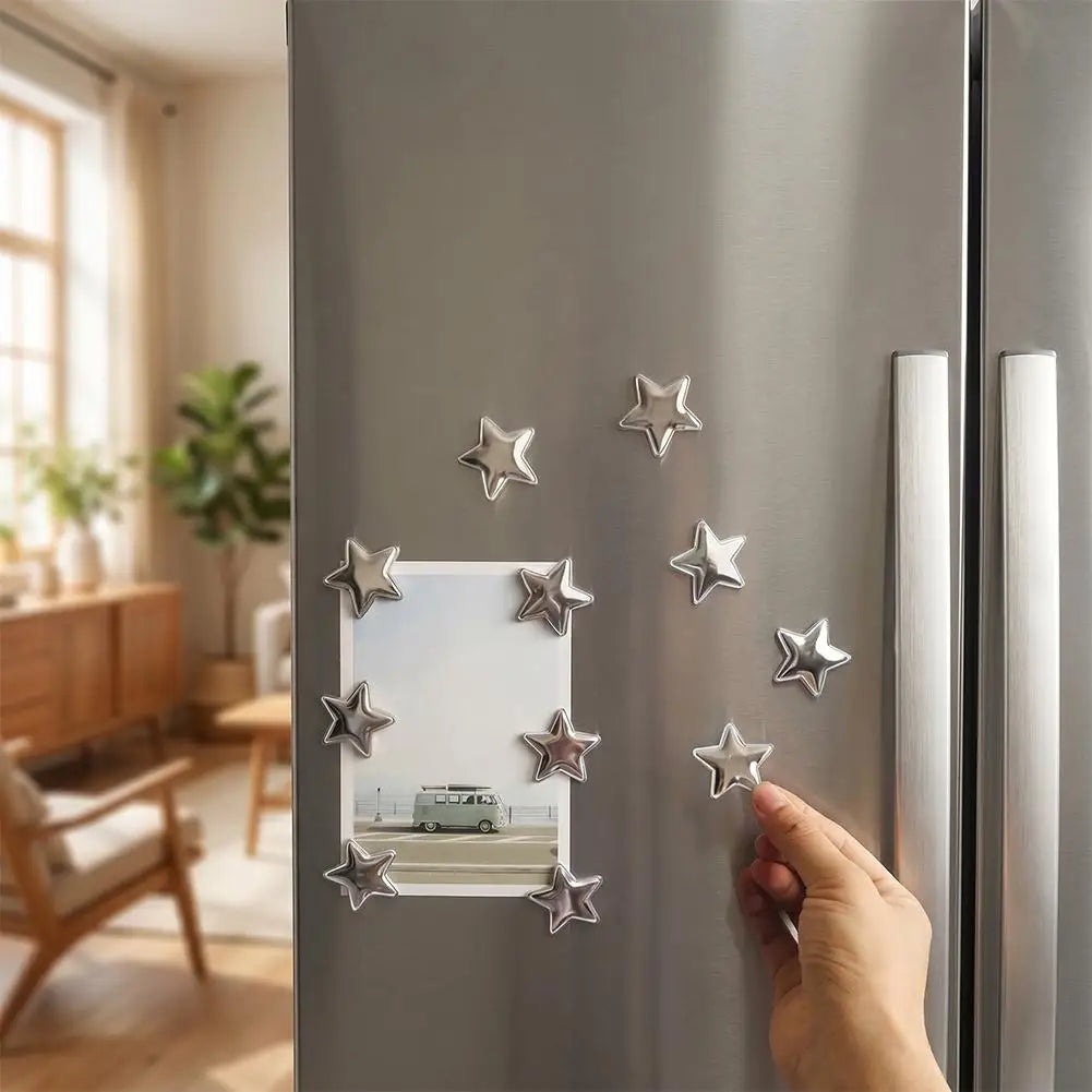 A hand places a silver star magnet onto the door of a stainless steel refrigerator.