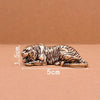 A vintage brass tiger figurine statue lying down on a brown surface.