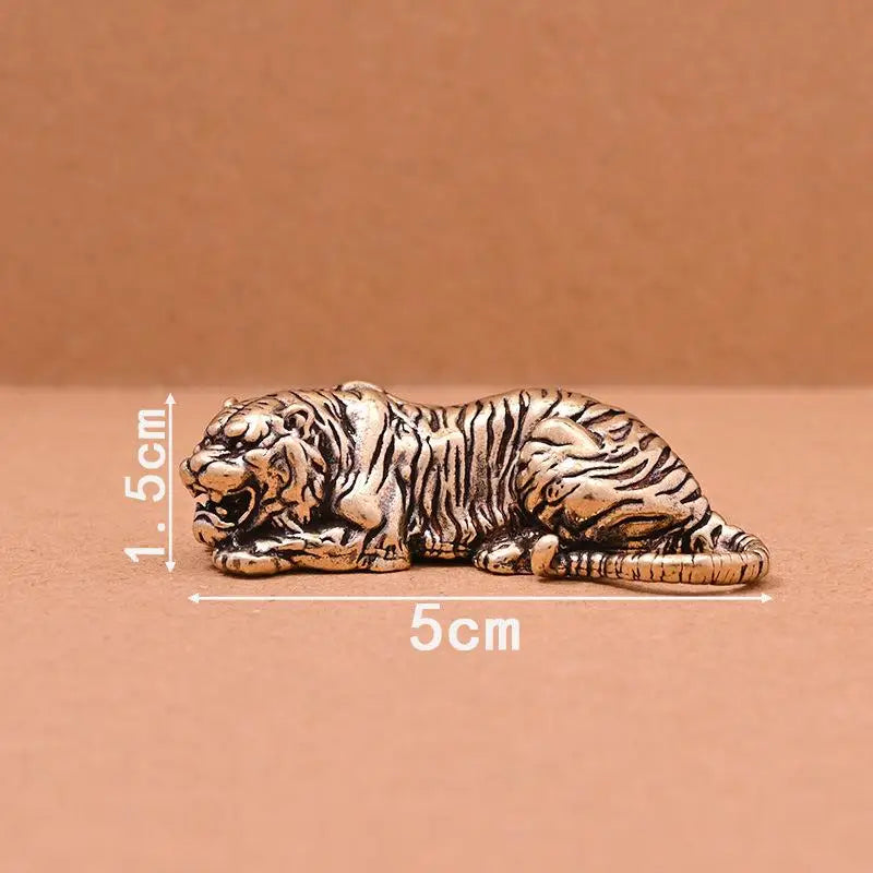 A vintage brass tiger figurine statue lying down on a brown surface.