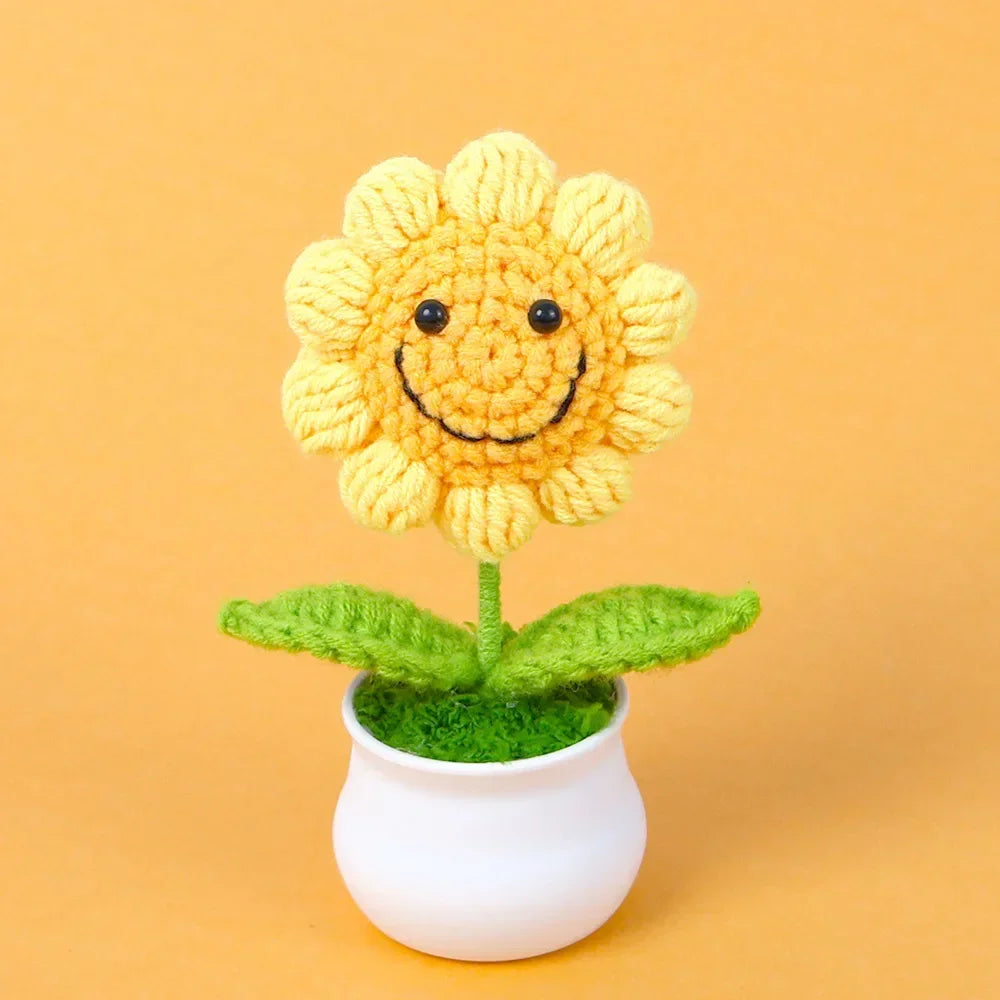 Handmade knitted yellow sunflower with green leaves growing in a white pot