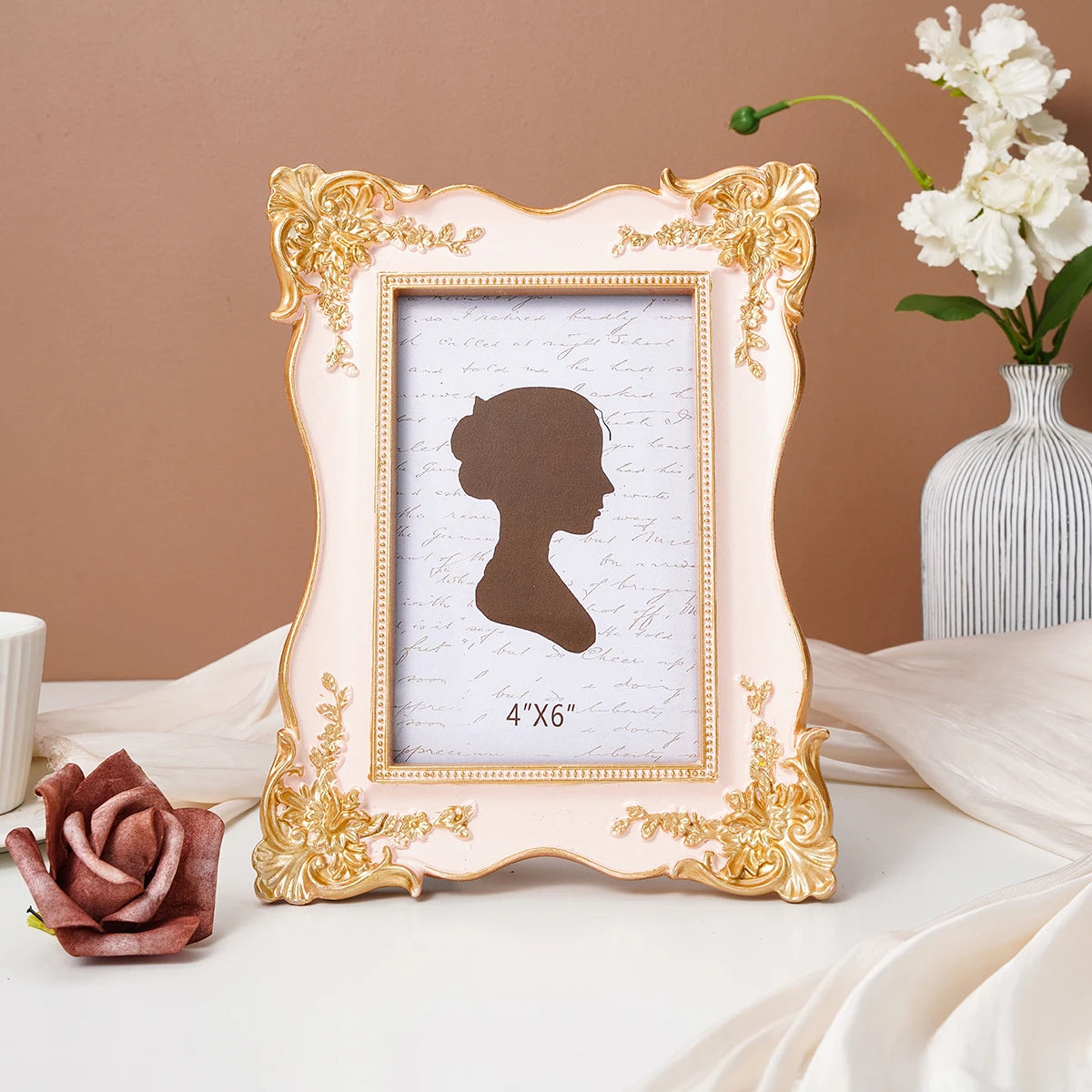 A delicate gold-framed photo frame with a light pink background and a silhouette of a woman's profile.