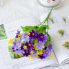 A close-up of purple and yellow artificial daisy flowers arranged in a green leafy bouquet on a page of a book.