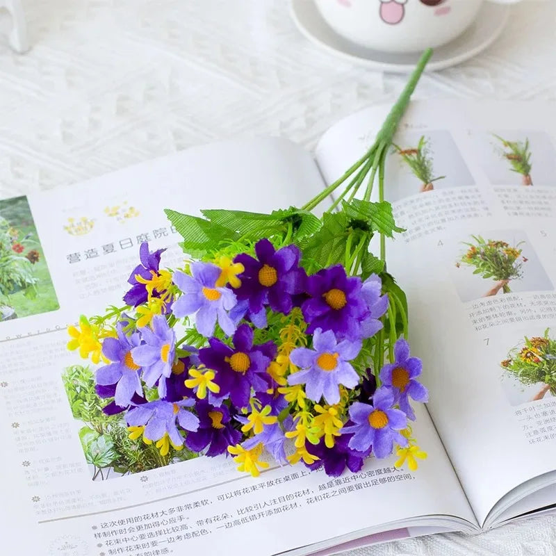 A close-up of purple and yellow artificial daisy flowers arranged on a white page, likely for decorative purposes.