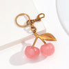A gold-toned pendant keychain shaped like a pink cherry made of resin.