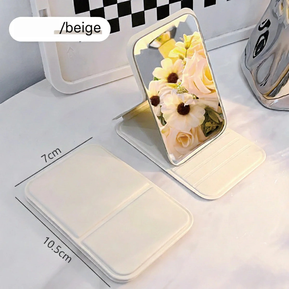 A beige portable folding HD makeup mirror with a floral arrangement is shown on a white surface.