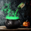 A black witch cauldron emitting green fog mist on a wooden surface.