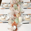 An artificial maple leaf vine garland centerpiece featuring white pumpkins and rustic cutlery on a white tablecloth.