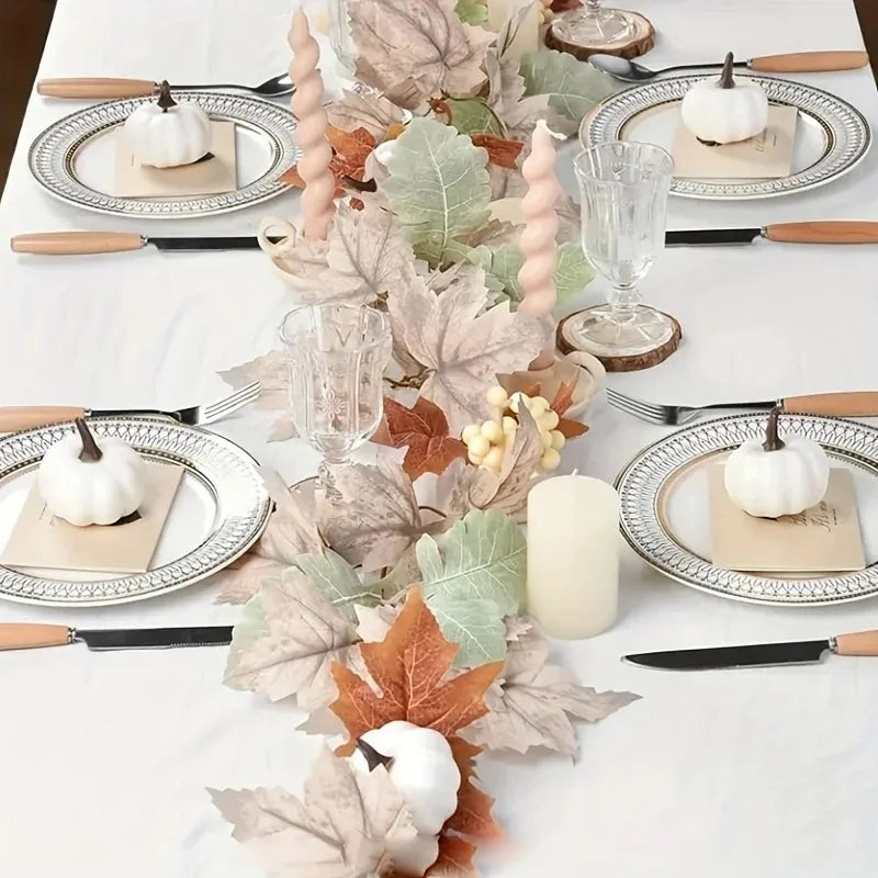 An artificial maple leaf vine garland centerpiece featuring white pumpkins and rustic cutlery on a white tablecloth.