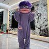 A purple, fuzzy monster coral fleece hooded sleepsuit with large eyes and a pink mouth standing in a modern room.