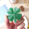 A hand holds a green natural aventurine quartz four-leaf clover crystal statue.