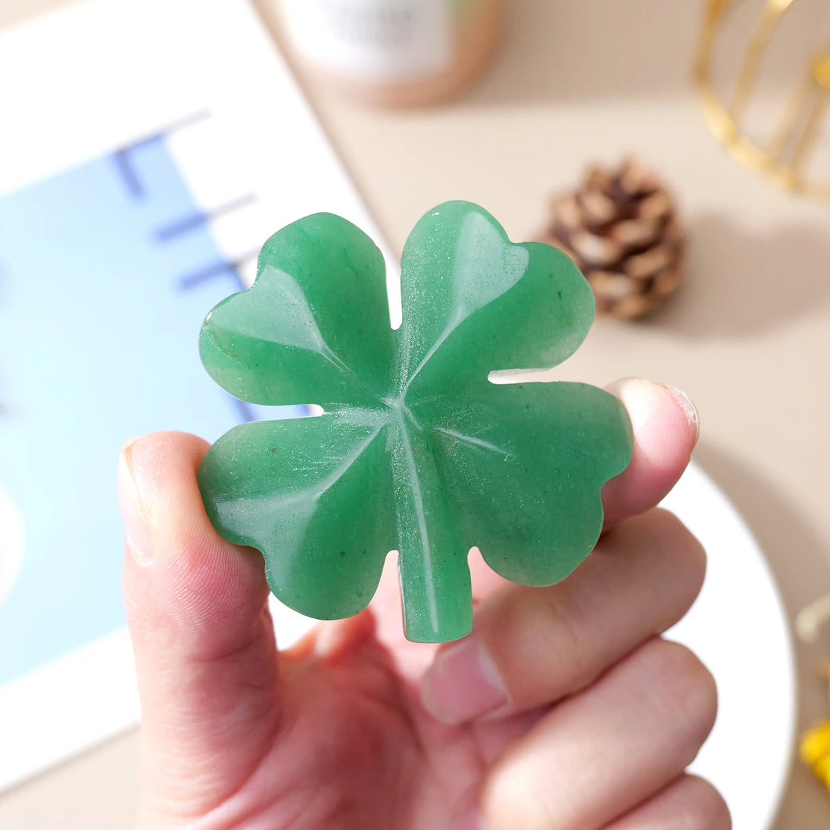 A hand holds a green natural aventurine quartz four-leaf clover crystal statue.