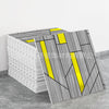 A stack of gray and white marble peel-and-stick tiles with yellow accents displayed on a gray floor.