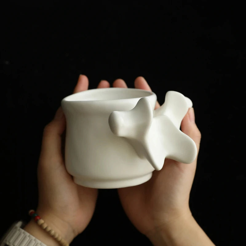 A person holds a white ceramic vase shaped like vertebrae against a dark background.