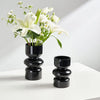 A black glass flower vase filled with white lilies and greenery on a white surface.
