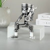 A silver mechanical piston skull sculpture is displayed on a white rectangular stand.