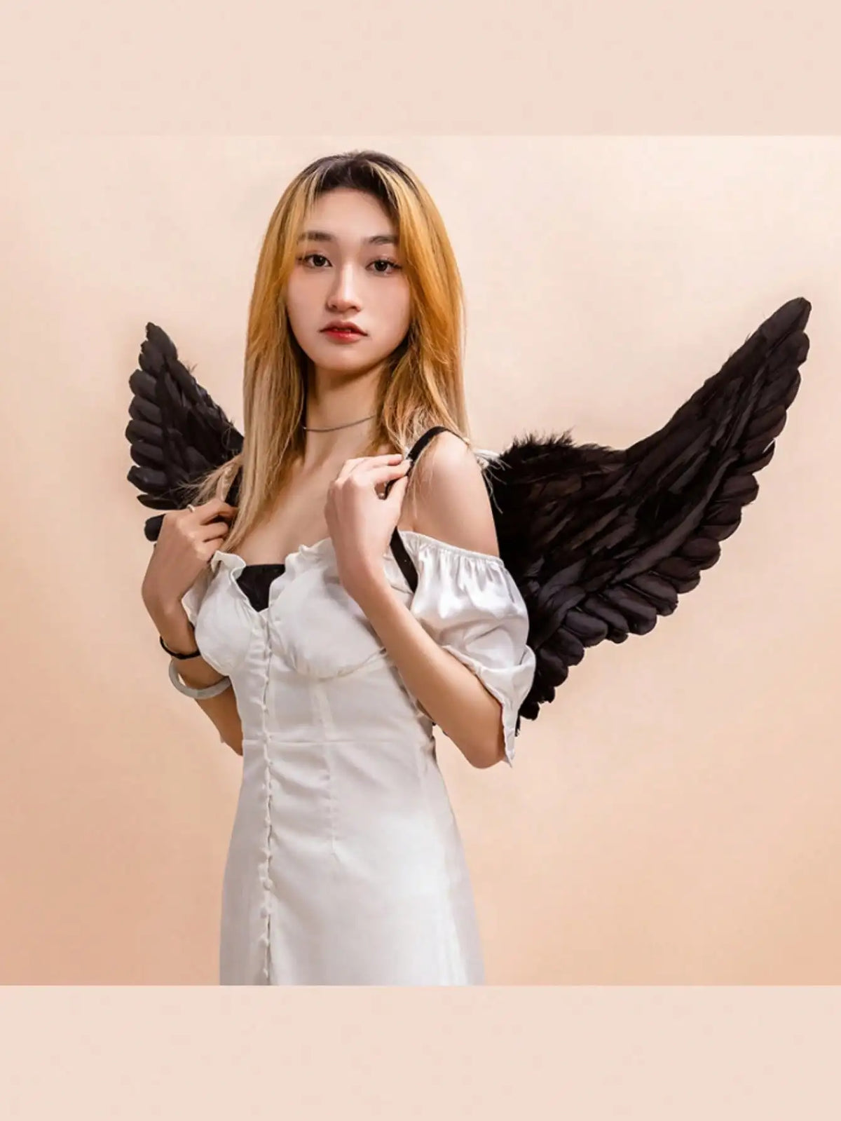 A woman wearing a white angel costume with large black feather wings against a light background.