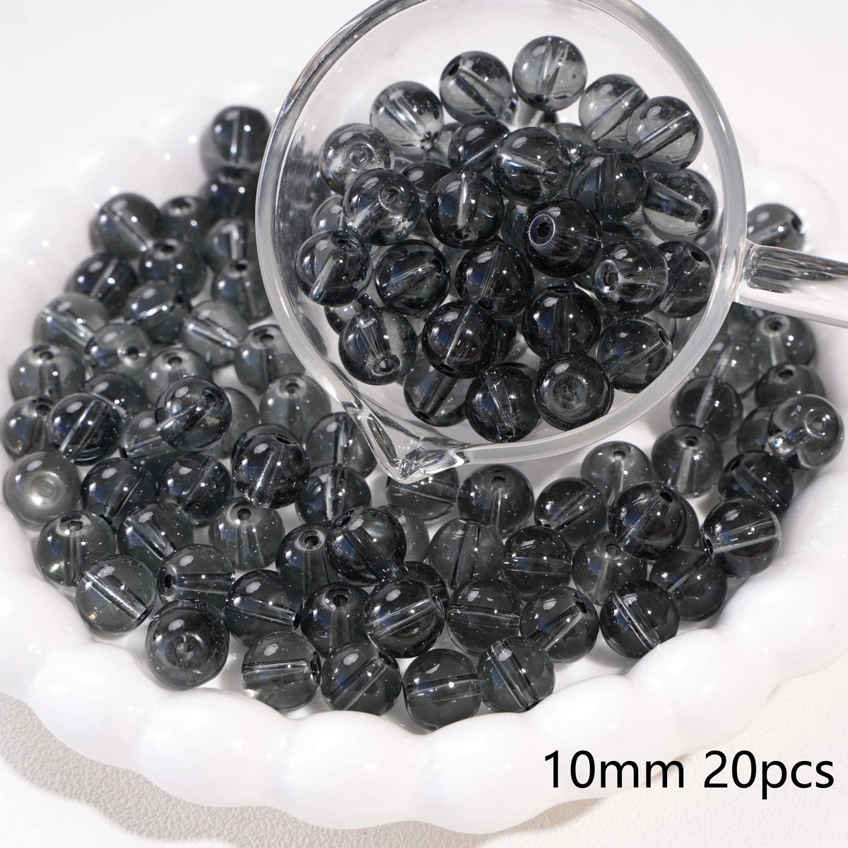 A clear glass container filled with small, dark gray spacer beads for jewelry making