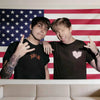 Two young men pose in front of an American flag tapestry wall art.