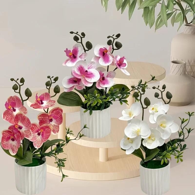 A cluster of pink and white artificial phalaenopsis orchids in white pots displayed on a wooden surface.