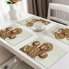 A set of four Christmas gingerbread man printed placemats with wooden utensils and a white teacup on a white table.
