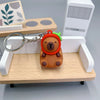 Pendentif de capybara orange avec accents verts, posé sur une étagère en bois clair.