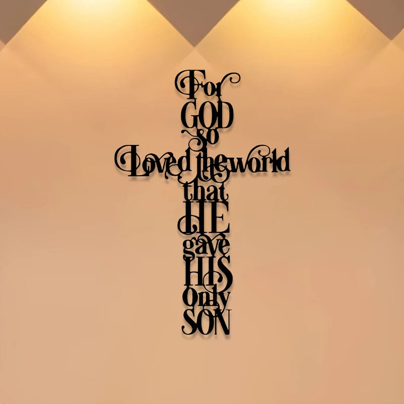 A black iron cross wall art featuring the quote For God So Loved the world that He gave His only Son mounted on a beige wall.