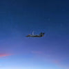 A military jet aircraft flying high in a dark blue night sky with faint stars and pink hues on the horizon.
