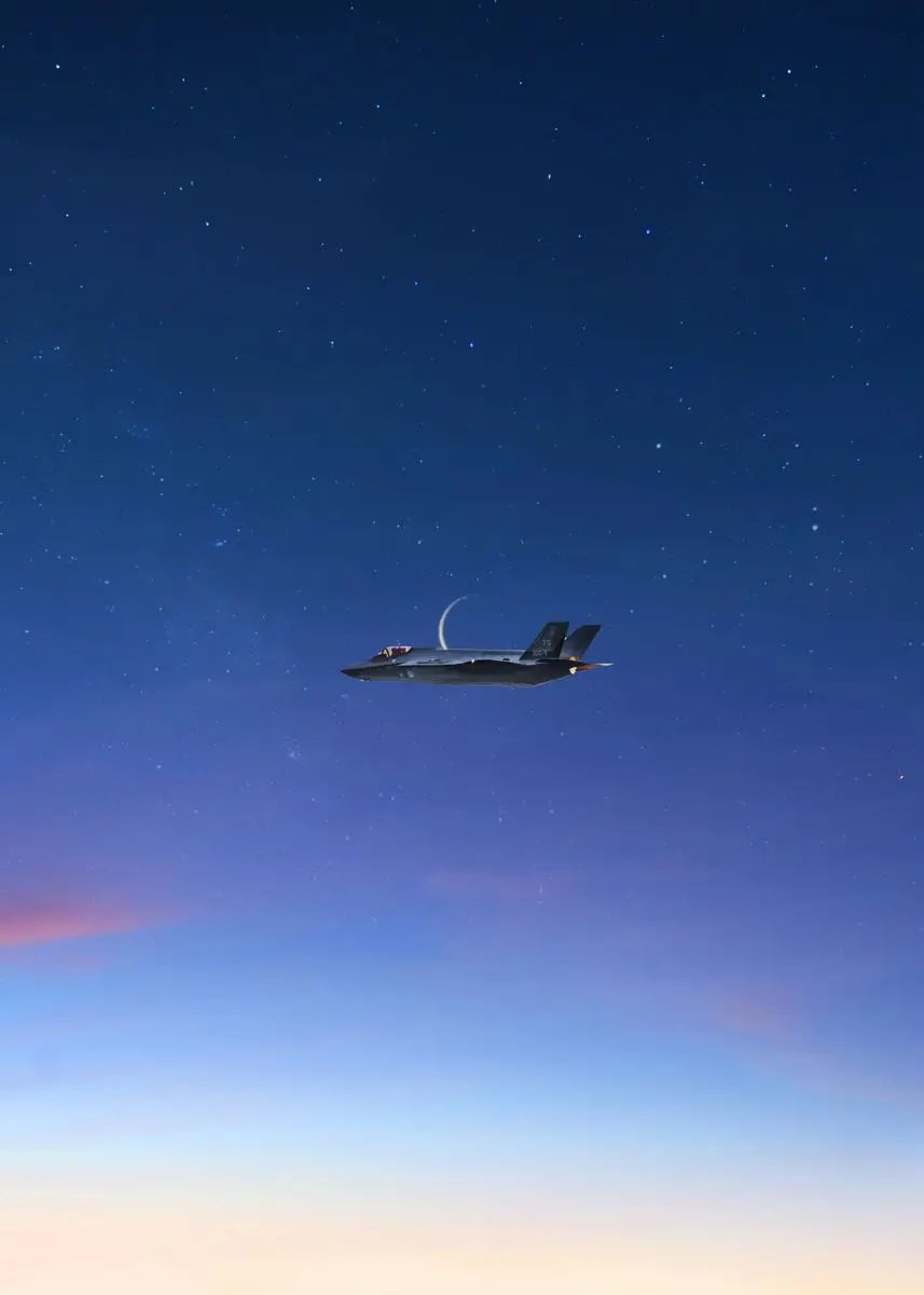 A military jet aircraft flying high in a dark blue night sky with faint stars and pink hues on the horizon.