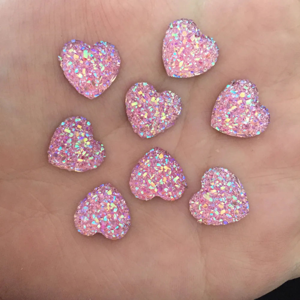 Eine Hand hält mehrere rosa glitzernde, herzförmige Strassornamente.