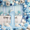 A large light blue foil number balloon shaped like the number one is surrounded by blue and silver balloons for a birthday ce