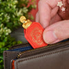 A hand holds an orange leather pouch with a gold tortoise figurine on the zipper pull.