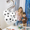 A woman and a young boy are posing with white latex football party balloons in a bright indoor setting.