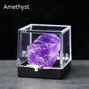 A rough amethyst crystal specimen displayed inside a clear glass box on a dark surface.