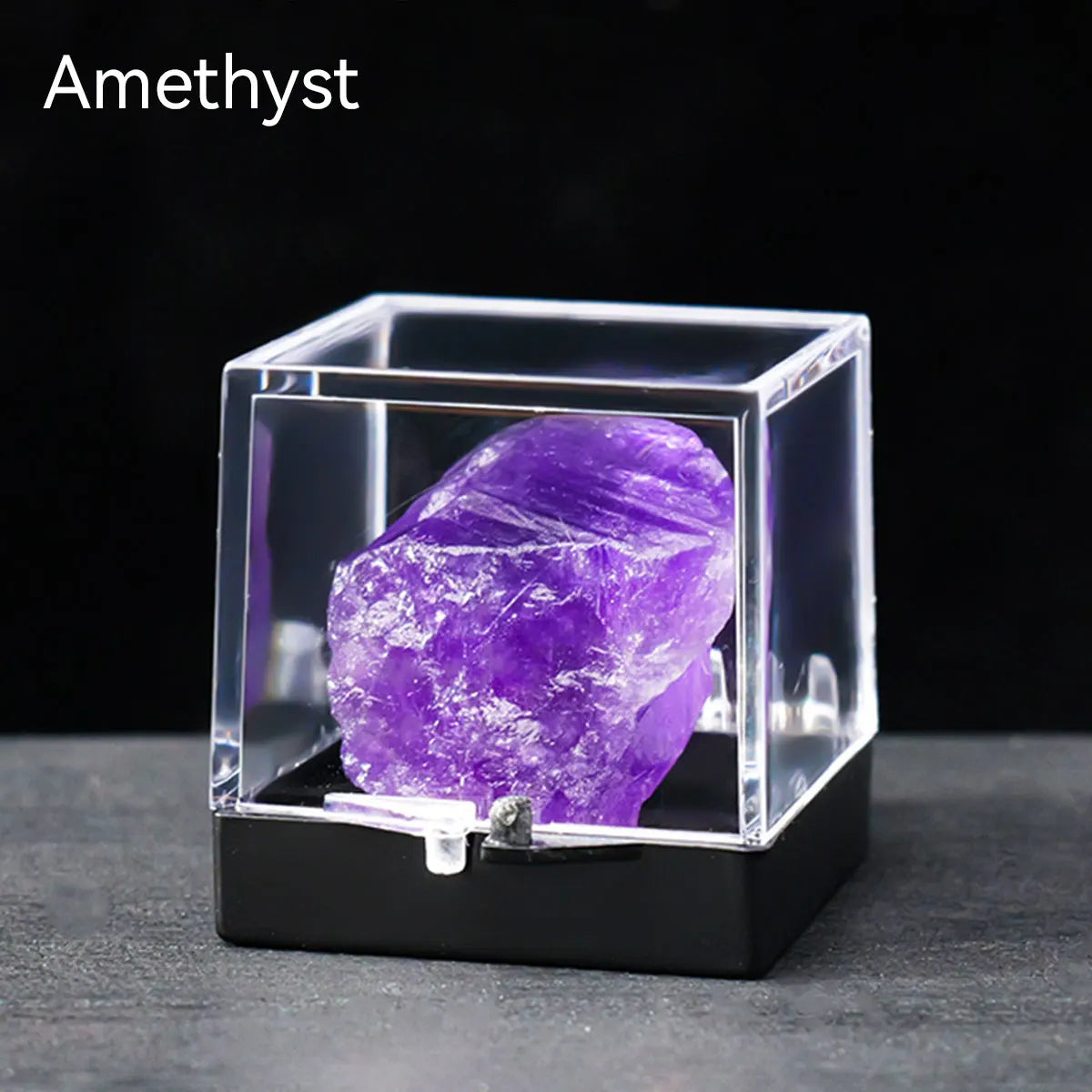 A rough amethyst crystal specimen displayed inside a clear glass box on a dark surface.