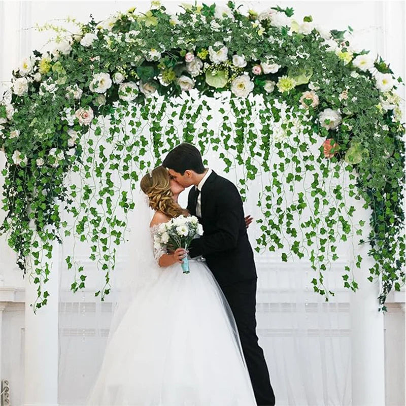 A bride and groom stand beneath a lush green ivy vine garland archway for a wedding photo.