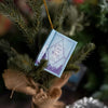 A book titled The Call of the Wild is hanging from a green pine branch with a gold string.