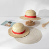 A straw hat with a red band is displayed on a wooden stand next to a flat straw hat.