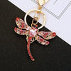 Gold-toned crystal dragonfly keychain featuring pink and gold accents on a black background.