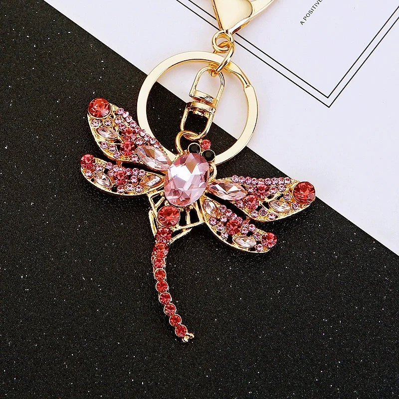 Gold-toned crystal dragonfly keychain featuring pink and gold accents on a black background.