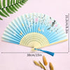 A light blue bamboo folding hand fan with floral accents and a blue tassel displayed on a pink background.