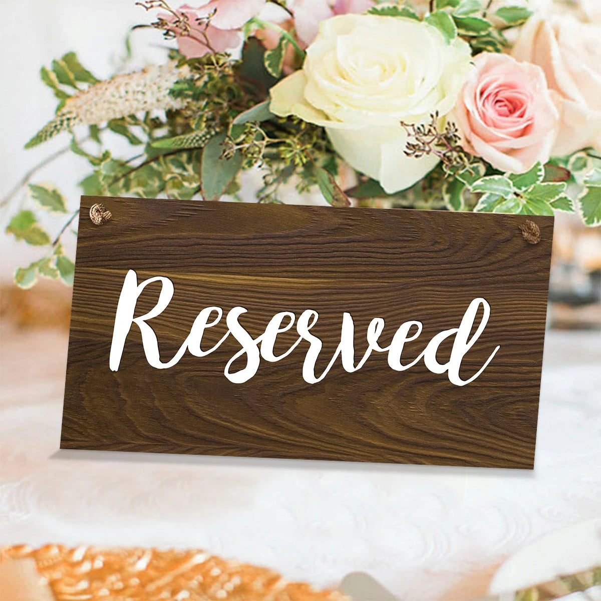 A dark wooden sign with the word Reserved written in white script, set against a backdrop of floral arrangements.