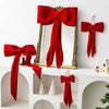 A set of twelve red velvet Christmas tree bow ornaments displayed on a white shelf with a mirror.