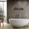 Une baignoire ovale blanche moderne devant un mur gris texturé avec des crochets de serviettes en métal noir.