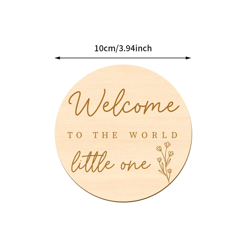 A round wooden sign with the text Welcome to the world little one engraved on it.