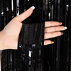 A hand holds a black metallic tinsel foil fringe curtain backdrop for parties.