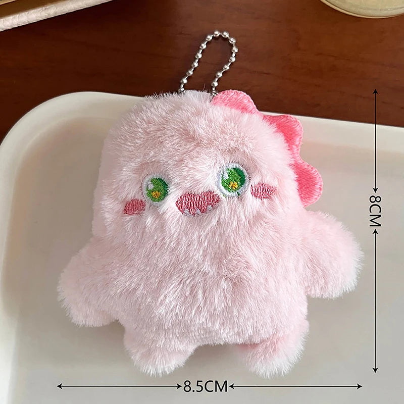 A soft pink fuzzy plush monster keychain with embroidered features resting on a white surface.