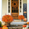 An artificial autumn floral decoration set featuring orange and yellow flowers displayed on a porch with pumpkins.