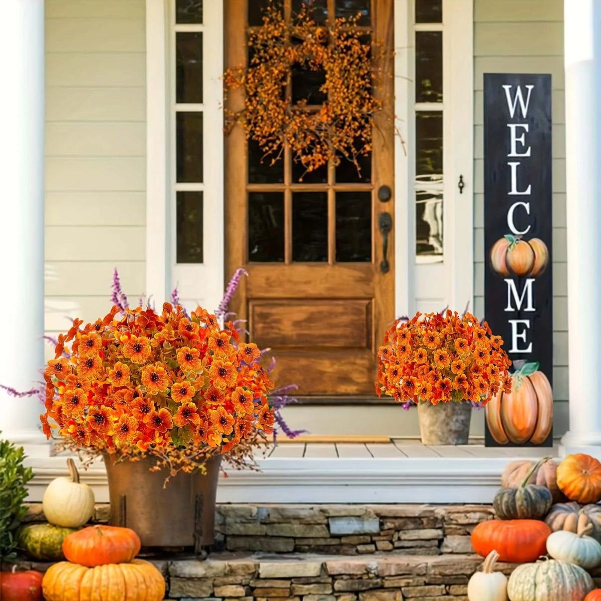 An artificial autumn floral decoration set featuring orange and yellow flowers displayed on a porch with pumpkins.