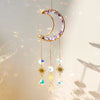 A golden crescent moon dreamcatcher with purple crystals and hanging prism charms against a soft light background.